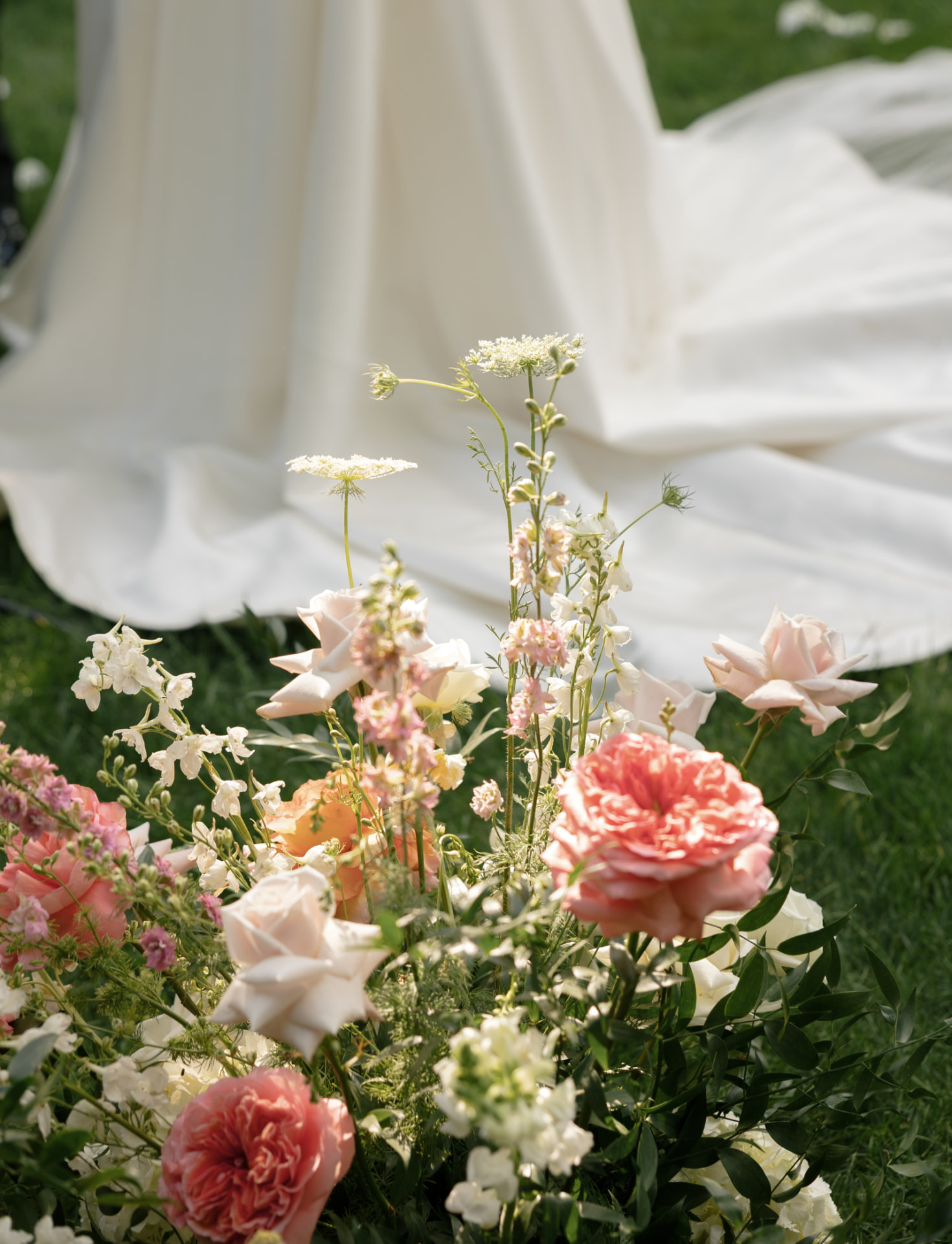 Blush wedding flowers arranged beside a bride's gown